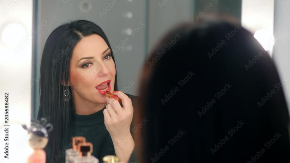 Reflection of lady applying her make-up. Brunette mature woman putting lipstick while looking in mirror. Makeup at night getting ready before going to party. Slow motion Reflection of lady applying her make-up. Brunette mature woman putting lipstick while looking in mirror. Makeup at night getting ready before going to party. Slow motion