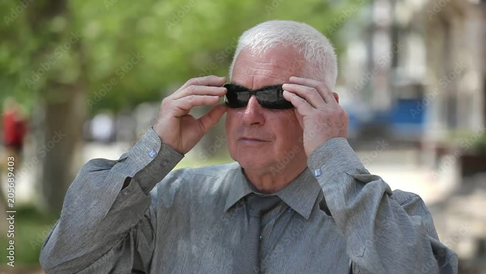 Portrait of a white-headed man putting on fashionable sunglasses and putting his short hair in order optimistically in a city park in summer Portrait of a white-headed man putting on fashionable sunglasses and putting his short hair in order optimistically in a city park in summer