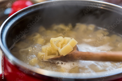 Heart shaped pasta cooked in red pot with white dots on stove. Meal prepared with love. 