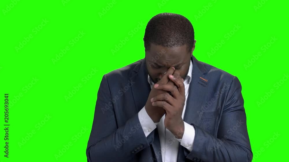 Unhappy businessman is crying on green screen. Depressed afro american entrepreneur on Alpha Channel background. Regrretting about something. Young dark-skinned man is praying. Unhappy businessman is crying on green screen. Depressed afro american entrepreneur on Alpha Channel background. Regrretting about something. Young dark-skinned man is praying.