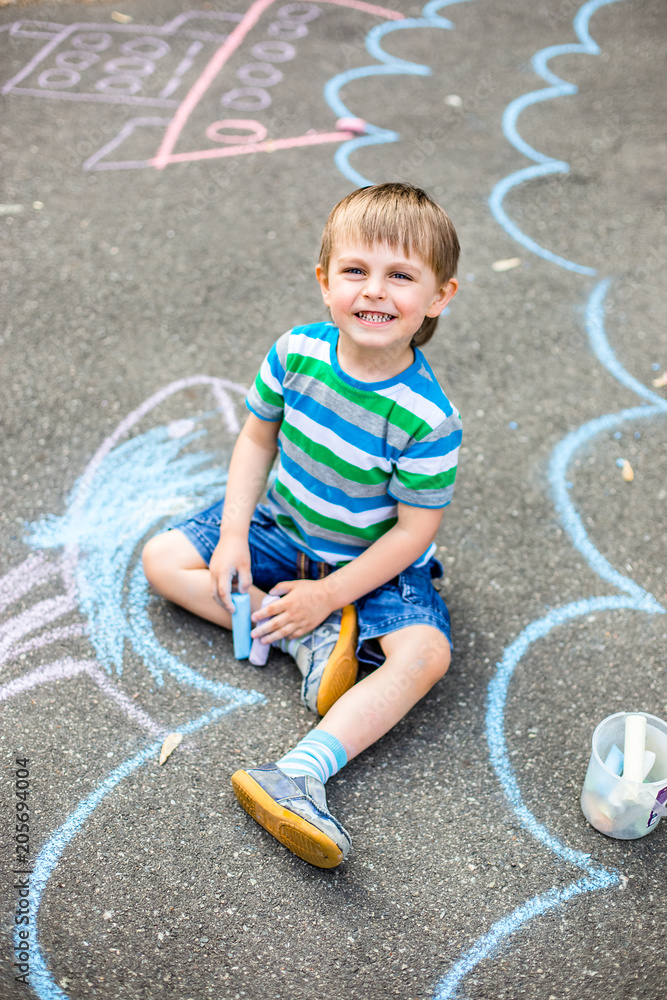 Fototapeta premium Cute boy and girl drawing with chalk on the sidewalk in the park.