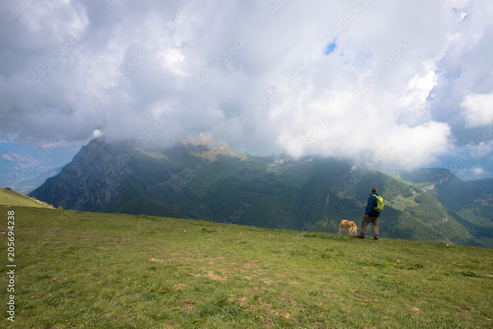 Panorama of the gorgeous alps mountains and hiker with dog on Monte Baldo mountain and white clouds Macesine, Provincia di Verona, Veneto, Italy