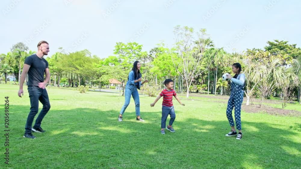 Family playing soccer in park in afternoon. German white male and asian woman with young boy, girl playing soccer together in park. Weekend family fun concept. Family playing soccer in park in afternoon. German white male and asian woman with young boy, girl playing soccer together in park. Weekend family fun concept.