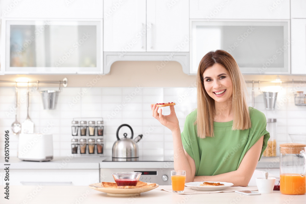 Beautiful woman eating tasty toasted bread with jam in kitchen Beautiful woman eating tasty toasted bread with jam in kitchen