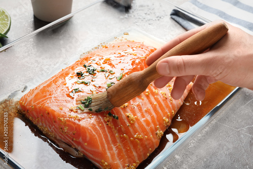Tableau sur toile Woman marinating raw salmon in dish at table