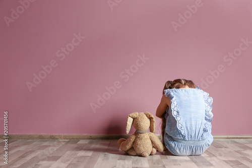 Fototapeta Naklejka Na Ścianę i Meble -  Little girl with toy sitting on floor near color wall in empty room. Autism concept