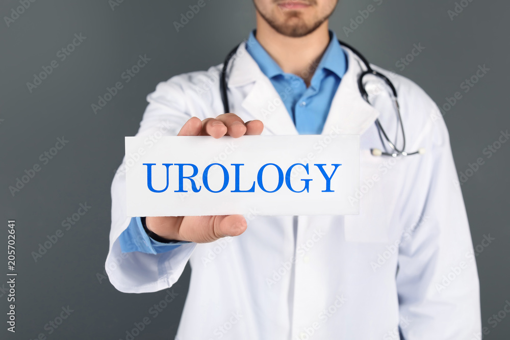 Male doctor holding paper with word UROLOGY on grey background Male doctor holding paper with word UROLOGY on grey background