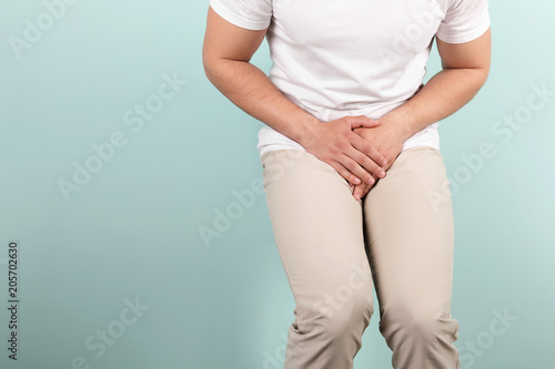 Young man with urological problems suffering from pain on color background