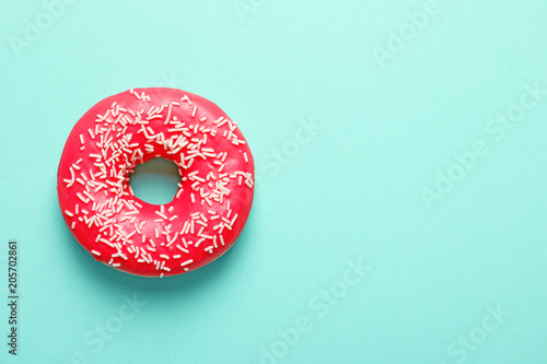 Delicious glazed doughnut with sprinkles on color background, top view