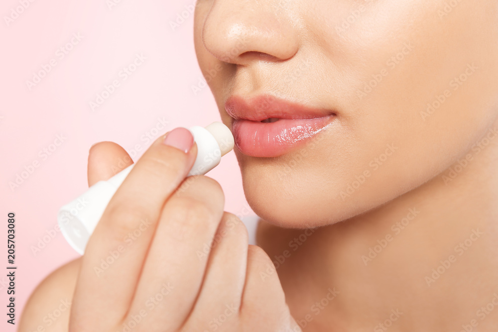 Young woman applying balm on her lips against color background, closeup Young woman applying balm on her lips against color background, closeup