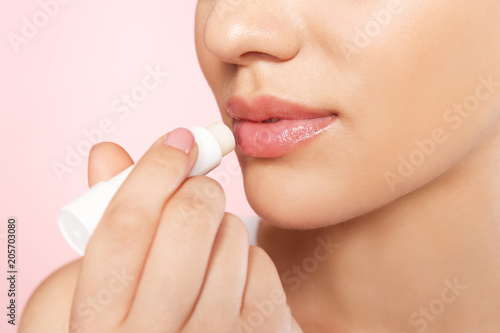 Young woman applying balm on her lips against color background, closeup photo