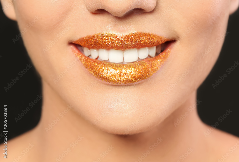 Fototapeta premium Beautiful young model with golden lips makeup on black background