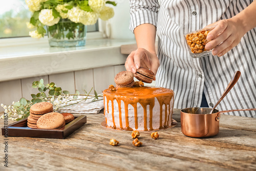 Young woman decorating delicious caramel cake at table