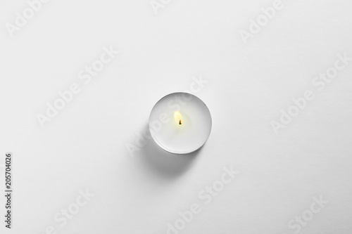Фотография Burning wax candle on white background, top view
