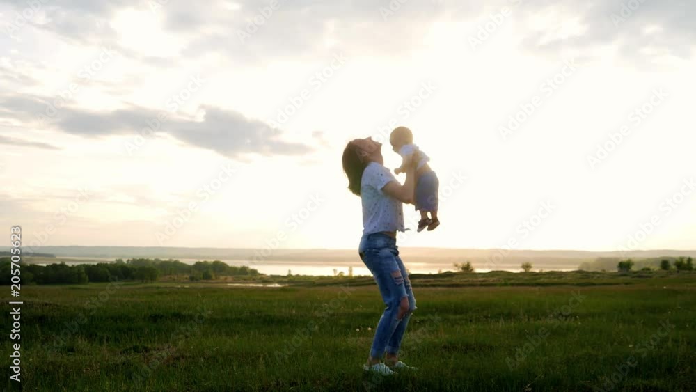 Mother and Baby having fun Outdoors. Mom throws up and catches her little son. Sun light, sunny day. Mother and Baby having fun Outdoors. Mom throws up and catches her little son. Sun light, sunny day.