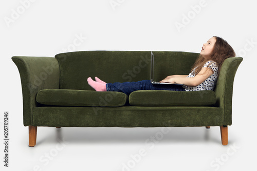 Cute little girl with voluminous hair relaxing at home, lying on green sofa with generic laptop computer, enjoying high speed wireless internet connection, playing video games online, feeling happy © Anatoliy Karlyuk