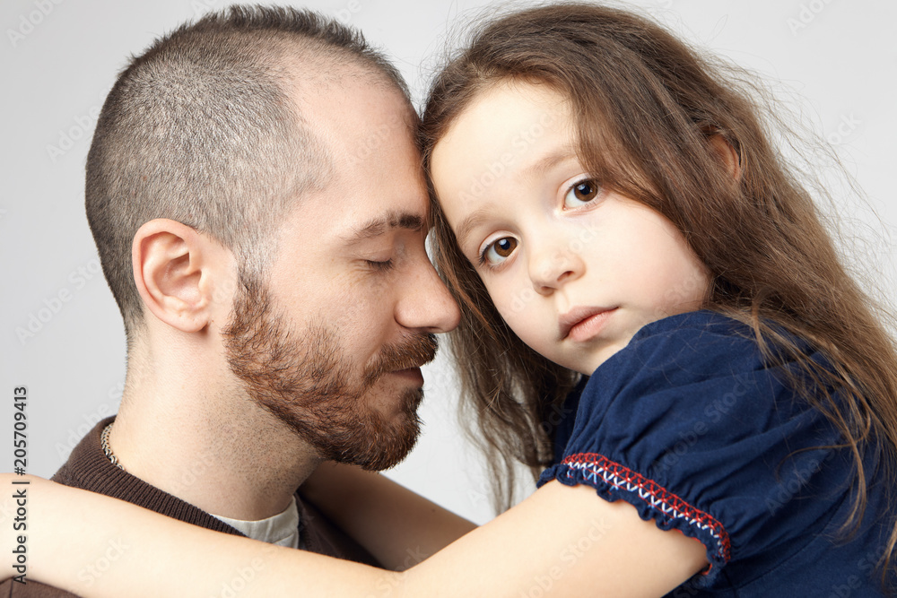 Love, family bonding and affection concept. Close up shot of attractive young Caucasian guy with stylish beard hugging his sad beautiful baby girl, closing eyes, expressing care and tenderness Love, family bonding and affection concept. Close up shot of attractive young Caucasian guy with stylish beard hugging his sad beautiful baby girl, closing eyes, expressing care and tenderness