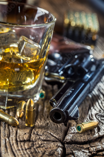 Glass of whiskey cognac or bourbon with revolver and bullets on wooden table