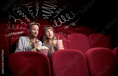 Young cute couple sitting in cinema, and eating popcorn while watching movie with doodle graphics © ra2 studio