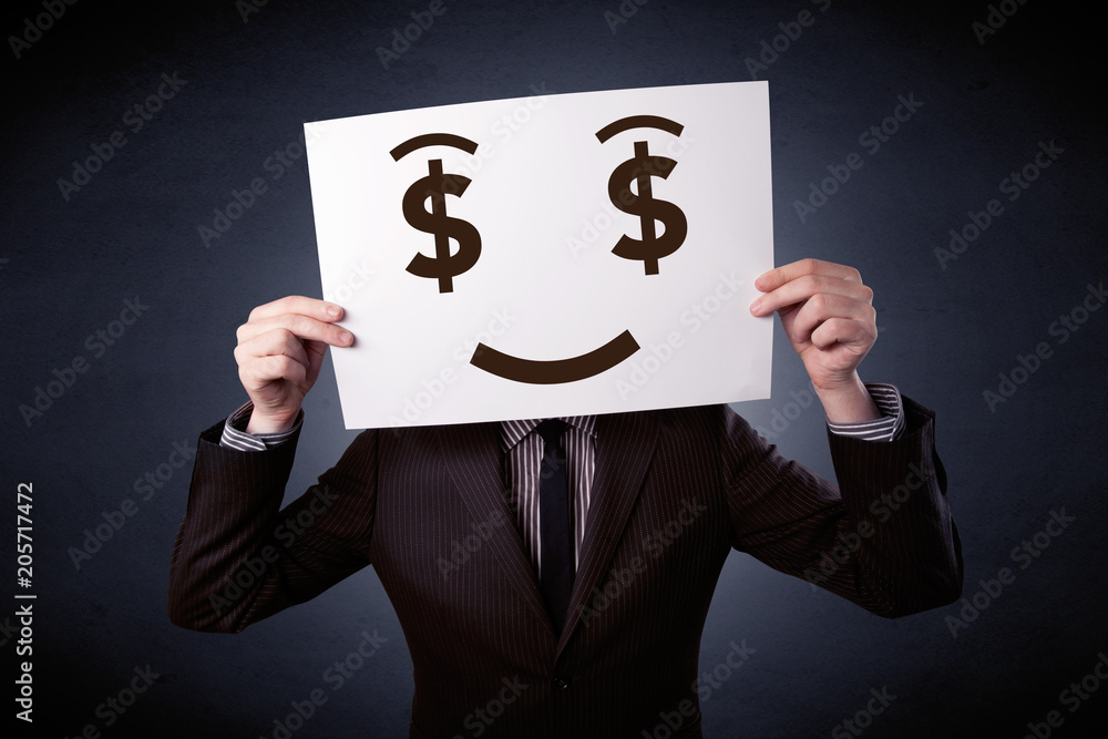 Young casual businessman hiding behind a greedy face drawing on cardboard Young casual businessman hiding behind a greedy face drawing on cardboard
