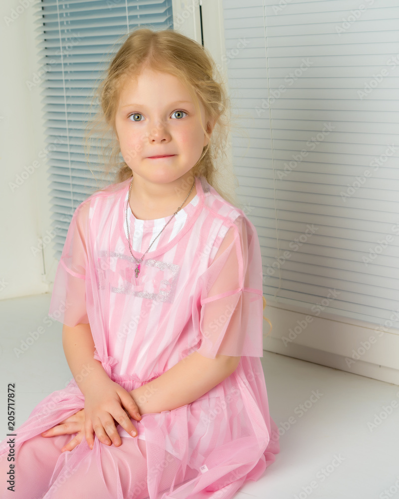 A little girl is sitting by the window with jalousie A little girl is sitting by the window with jalousie