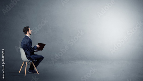 Businessman staying in an empty grey dark room with stuffs on his lap   © ra2 studio