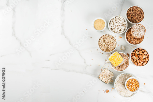 Selection various types cereal grains groats  in different bowl on white marble background, above copy space photo