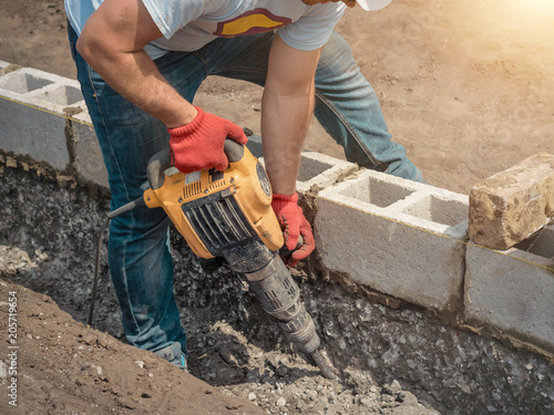 Bild auf Leinwand Worker with a jackhammer, foundation, building blocks.
