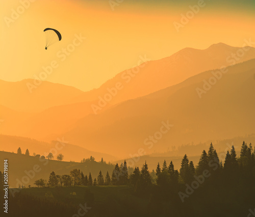 Silhouette of flying paraglider over the mountains
