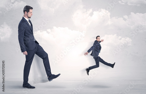 Big businessmen kicking himself as a small employee with cloudy background
