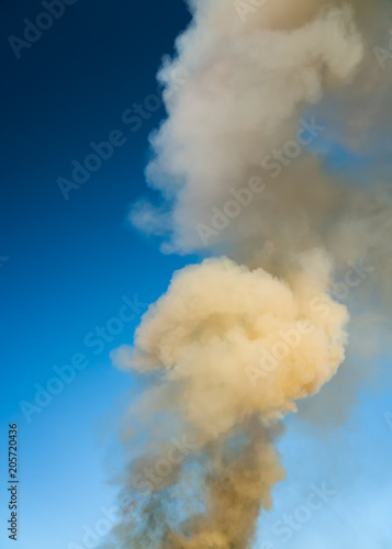 Closeup photo of heavy smoke on the clear blue sky background without any clouds