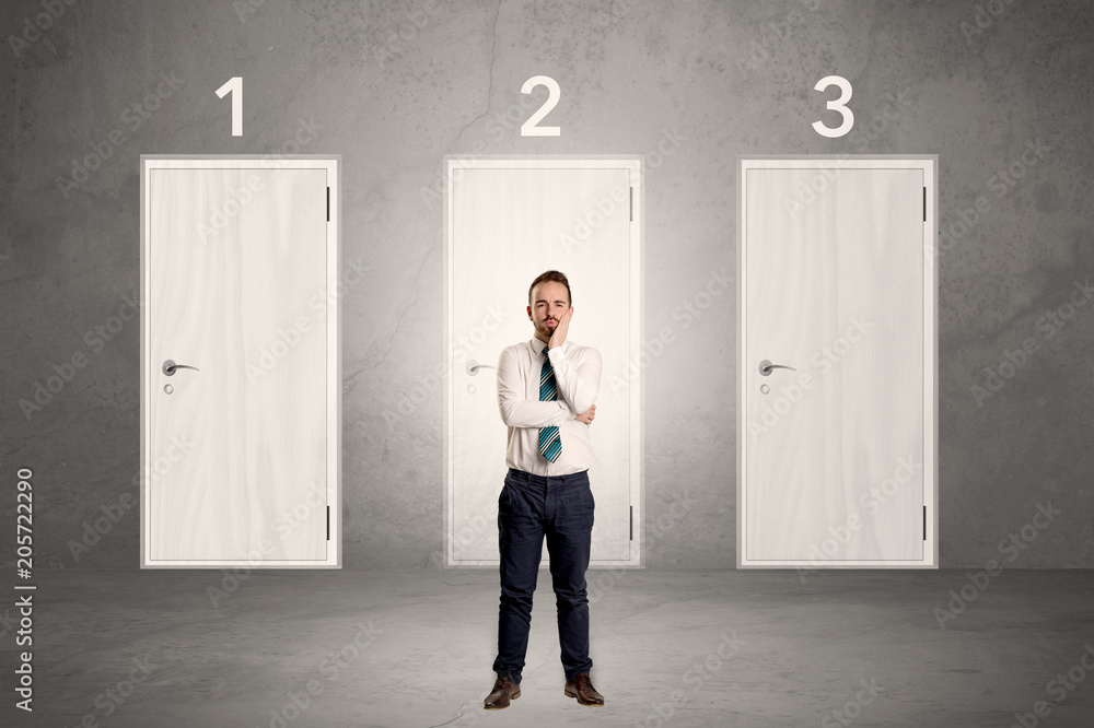 Fototapeta premium Businessman in grey room with three numbered white door behind his back 