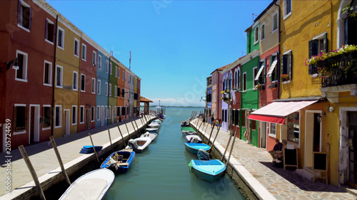 Colorful houses and boats moored along canal on Burano island, locals in street © motortion