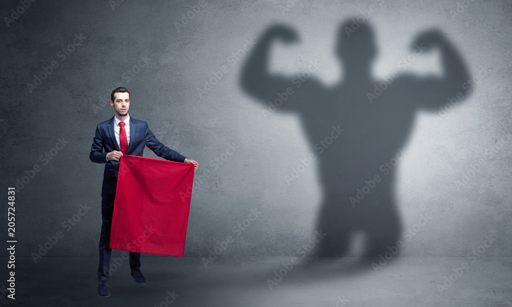 Obraz premium Businessman standing with red cloth on his hand and strong hero shadow on the background 