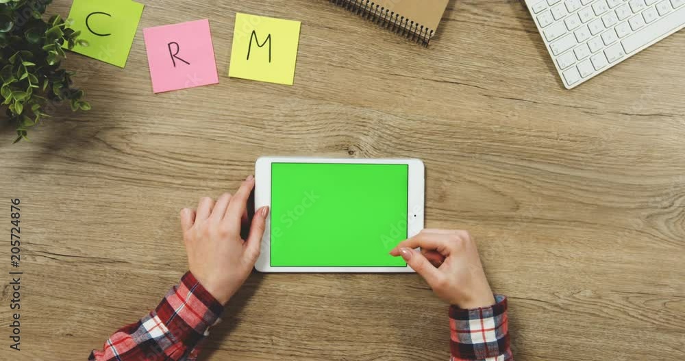 Close up on the woman's hands taping on the white horizontal tablet device with a green screen on the wooden table. SRM. Chroma key. Close up on the woman's hands taping on the white horizontal tablet device with a green screen on the wooden table. SRM. Chroma key.