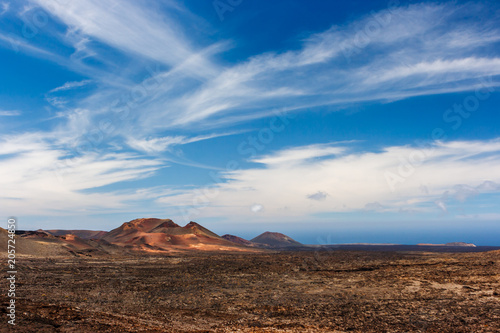 Volcanic crater in the Timanfaya National Park under a blue sky with clouds. Lanzarote, Canary Islands, Spain.