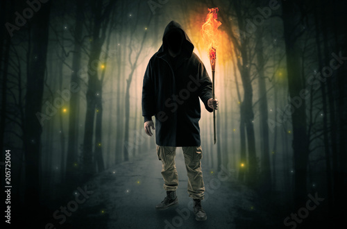 Mysterious man coming from a path in the forest with burning flambeau concept  