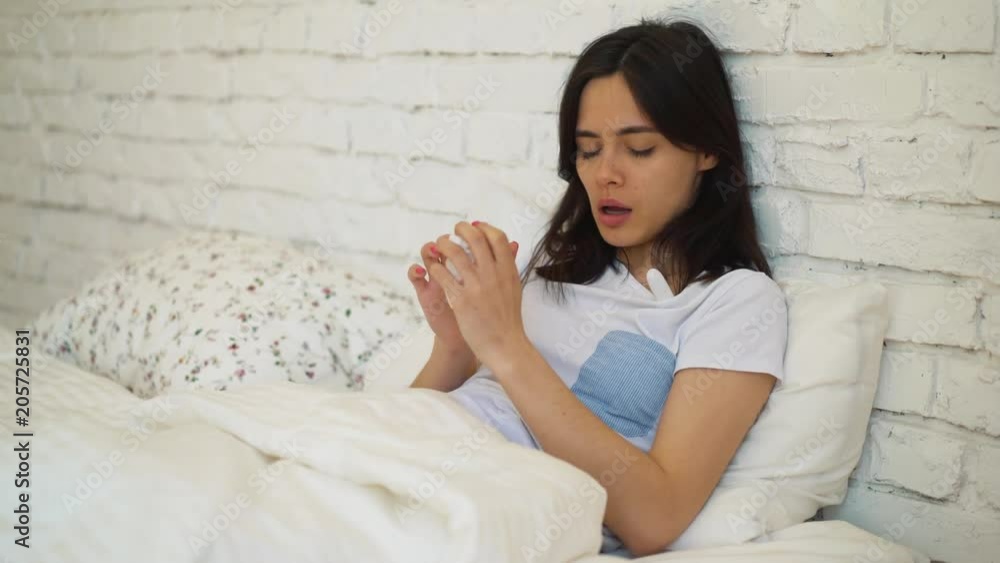 Girl is sitting on the bed she got sick this morning and wants to recover as soon as possible. Young woman will take some medicine to feel better later Girl is sitting on the bed she got sick this morning and wants to recover as soon as possible. Young woman will take some medicine to feel better later
