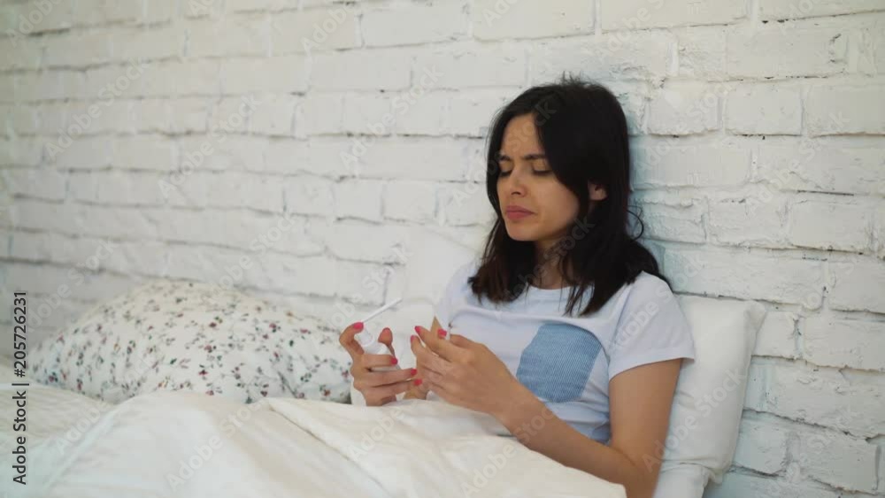 Girl is sitting on the bed she got sick this morning and wants to recover as soon as possible. Young woman will take some medicine to feel better later