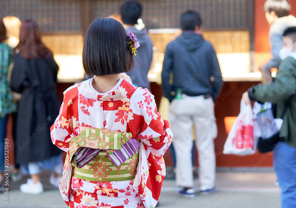 Obraz premium Young girl wearing Japanese kimono standing in front of Sensoji Temple in Tokyo, Japan. Kimono is a Japanese traditional garment. The word 