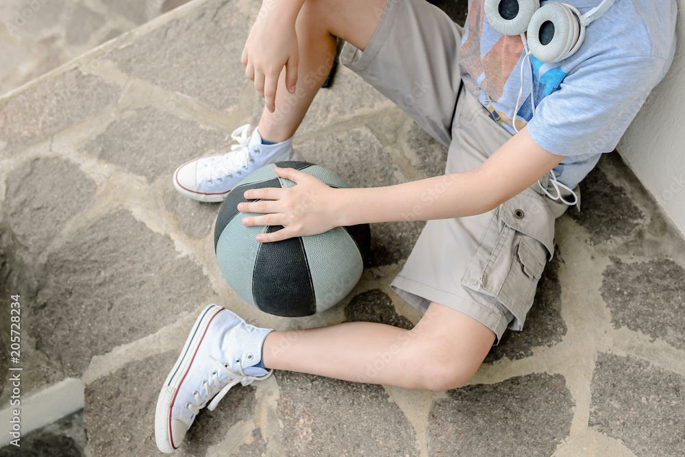 Young boy alone with shorts sitting after playing basket. Teen without ...