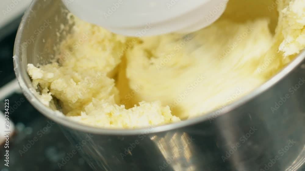 Process of preparing dough using kitchen processor in kitchen indoors. Electric mixer stirs yellow mass for baking in bowl on table in cuisine. Metal nozzle rotates, stirring sweet duff. Concept Process of preparing dough using kitchen processor in kitchen indoors. Electric mixer stirs yellow mass for baking in bowl on table in cuisine. Metal nozzle rotates, stirring sweet duff. Concept