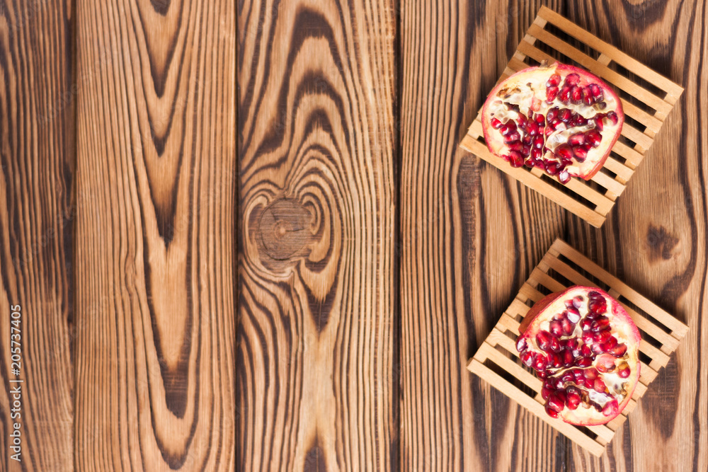 Two halves of red ripe fresh pomegranate on wooden pallets near scattered seeds on old brown weathered rustic planks. Top view Two halves of red ripe fresh pomegranate on wooden pallets near scattered seeds on old brown weathered rustic planks. Top view