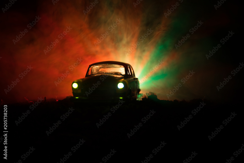 Silhouette of old vintage car in dark foggy toned background with glowing lights in low light, or silhouette of old crime car dark background.