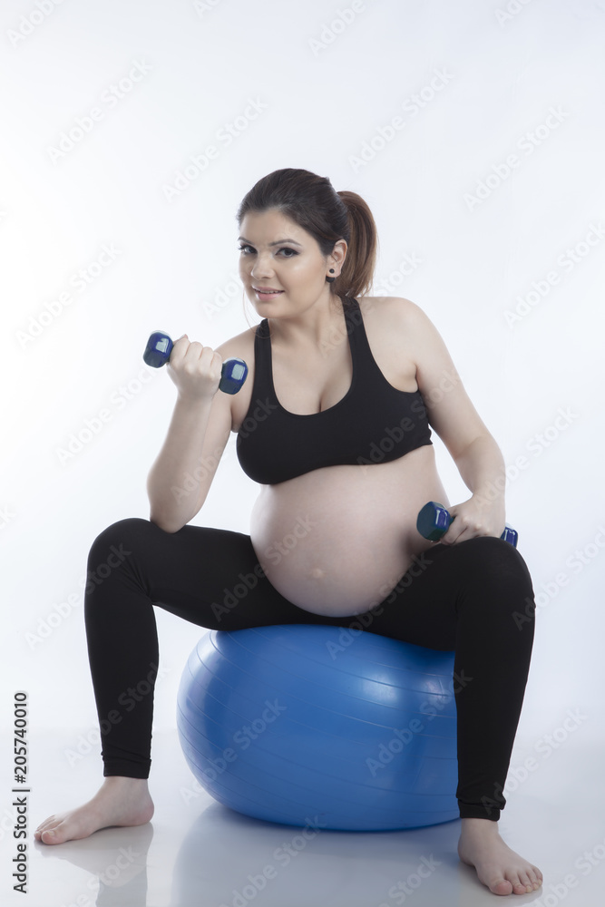 Pregnant woman is doing exercises with gymnastic ball on white background
