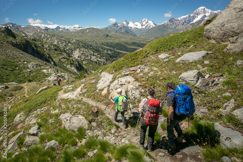 A family on a trip to the Italian Alps. Father, mother and son trekking on a beautiful summer day during mountain holidays. A mountain panorama with a family walking with backpacks with snow-capped pe