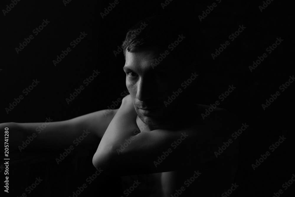 Black and white noir profile portrait of thoughtful handsome Caucasian topless male, tenderly touching his body, enjoying shape and fit, dreaming and resting in darkness. Fashion and beauty concept.