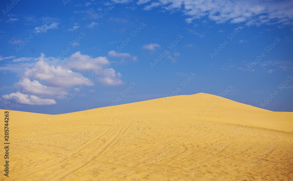 Naklejka premium Sand dunes near Mui Ne. Group of off roads on top of dunes in the background. Sunny day with blue sky and clouds