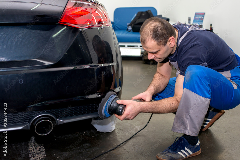 A man polishes a black car with a polisher A man polishes a black car with a polisher