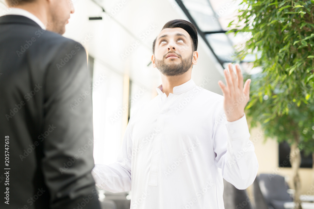 Young businessman looking upwards with raised hands while talking to his colleague about forthcoming event Young businessman looking upwards with raised hands while talking to his colleague about forthcoming event